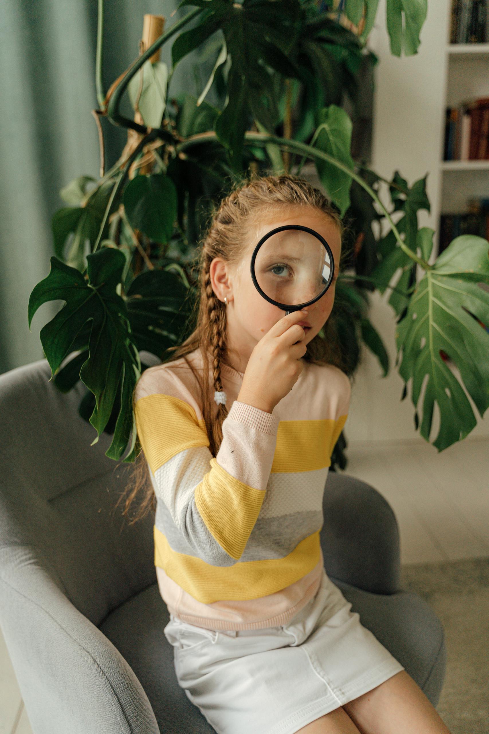 Young girl with magnifying glass in cozy indoor setting, exploring indoor plants with curiosity.